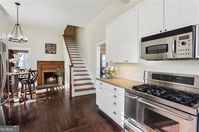 kitchen with a warm lit fireplace, stainless steel appliances, white cabinetry, light countertops, and dark wood-style floors