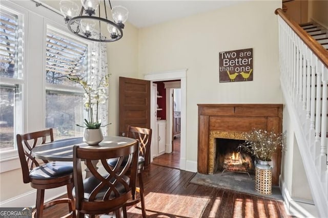 dining room with hardwood / wood-style flooring, a notable chandelier, a fireplace with flush hearth, baseboards, and stairs