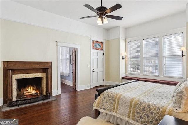 bedroom with a lit fireplace, wood finished floors, a ceiling fan, and baseboards