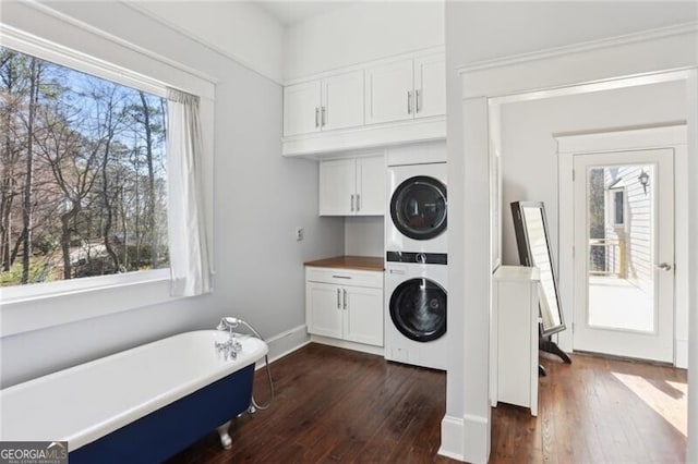 washroom with dark wood-style flooring, cabinet space, stacked washer and clothes dryer, and baseboards