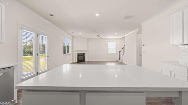 1069 Blue Juniper Cir, Loganville, GA 30052 - kitchen with a glass covered fireplace, a kitchen island, ornamental molding, white cabinetry, and stainless steel dishwasher