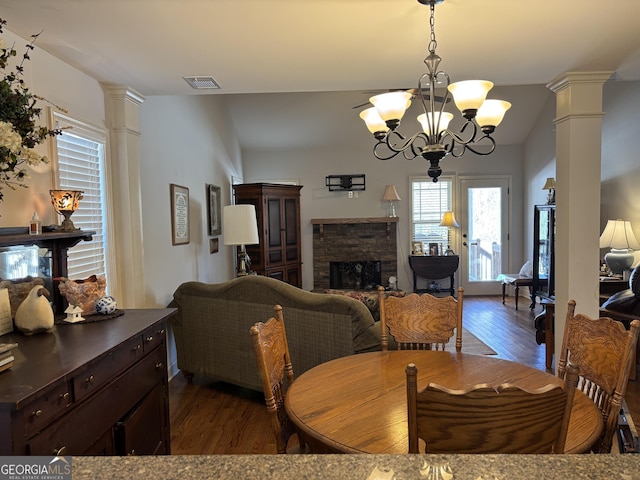 dining room featuring dark wood-type flooring, visible vents, decorative columns, and a stone fireplace