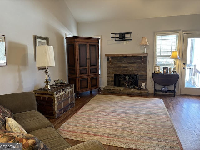 living area featuring a stone fireplace and dark wood-type flooring