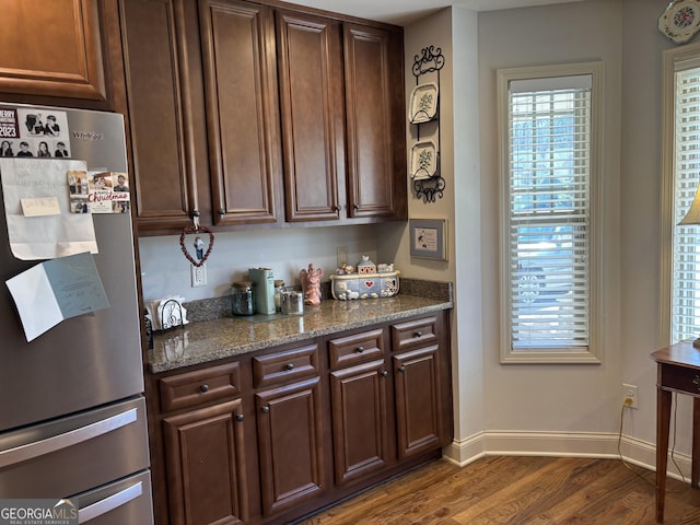 kitchen with dark wood-type flooring, baseboards, dark brown cabinets, freestanding refrigerator, and dark stone counters