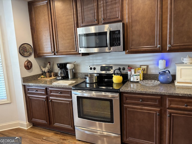 kitchen with stainless steel appliances, dark stone countertops, wood finished floors, and baseboards