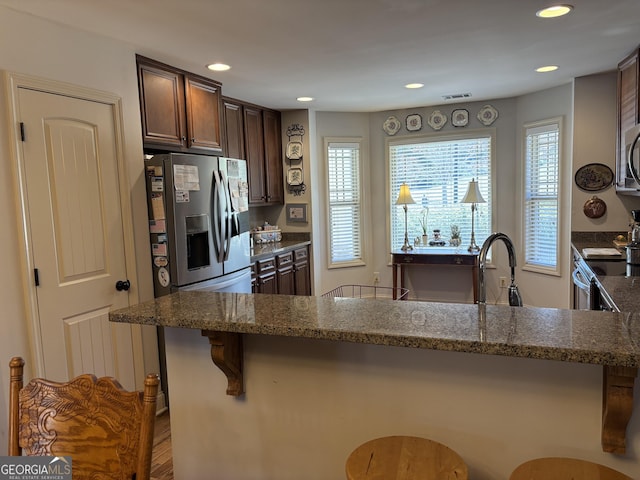 kitchen featuring visible vents, appliances with stainless steel finishes, a kitchen breakfast bar, and dark stone counters