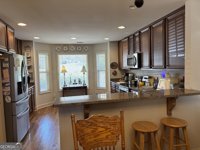 kitchen with stainless steel appliances, dark stone countertops, dark wood finished floors, and dark brown cabinetry