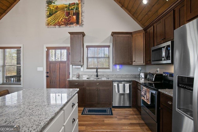 kitchen with dark wood finished floors, appliances with stainless steel finishes, a sink, light stone countertops, and wooden ceiling