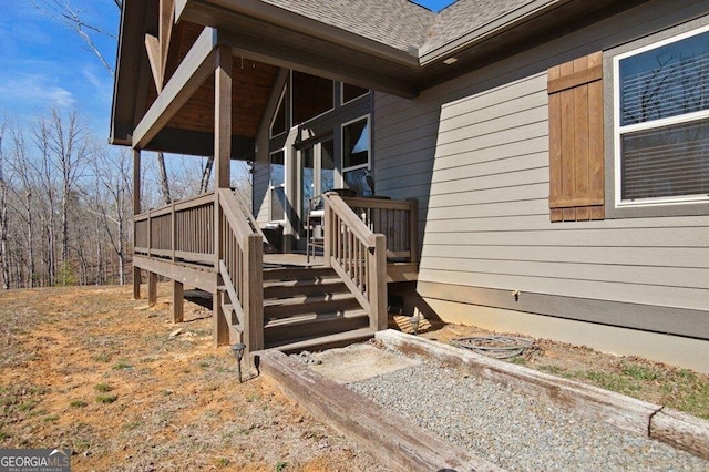 property entrance with a shingled roof and a wooden deck