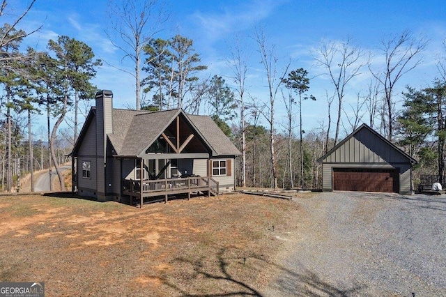 view of front of home with a detached garage, a chimney, a deck, board and batten siding, and a front yard