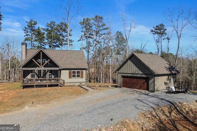 view of front of home with an outbuilding, a deck, a detached garage, roof with shingles, and a chimney