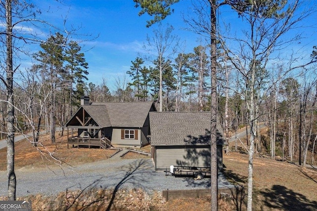 chalet / cabin featuring a deck, driveway, a shingled roof, and a chimney