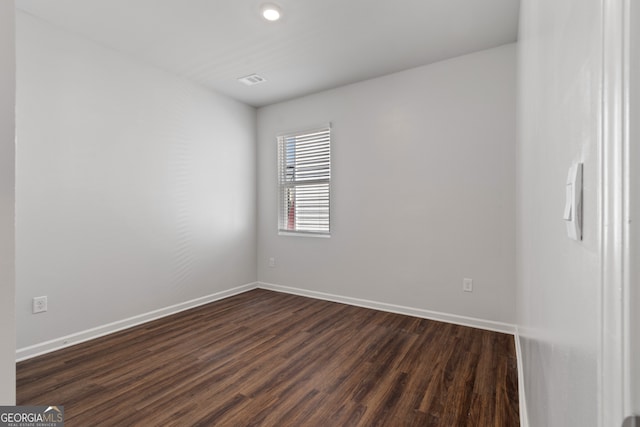 spare room with baseboards and dark wood-type flooring