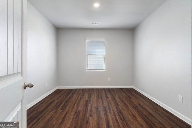 empty room featuring dark wood-type flooring, visible vents, and baseboards