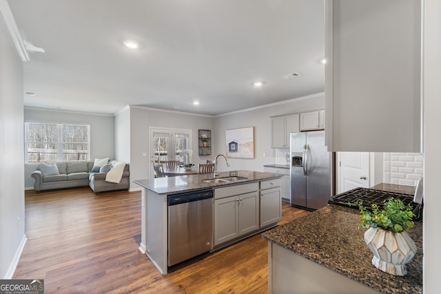 kitchen with a kitchen island with sink, stainless steel appliances, a sink, dark stone countertops, and dark wood finished floors