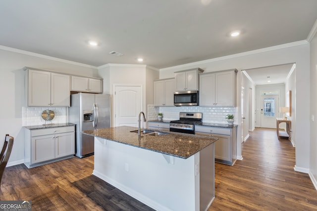 kitchen with gray cabinetry, stainless steel appliances, a sink, dark wood-style floors, and dark stone countertops