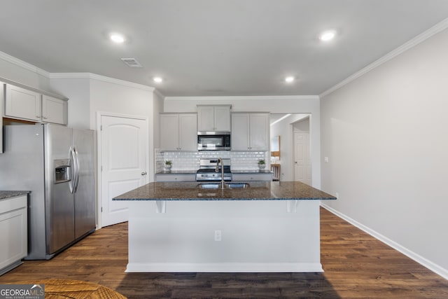 kitchen featuring dark wood-style flooring, appliances with stainless steel finishes, a kitchen island with sink, a sink, and dark stone counters