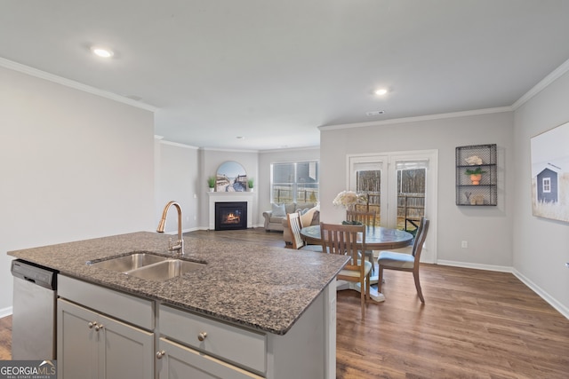 kitchen featuring dark wood-style flooring, a sink, dark stone countertops, a warm lit fireplace, and dishwasher