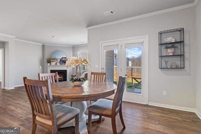 dining room with dark wood-type flooring, a warm lit fireplace, visible vents, and baseboards