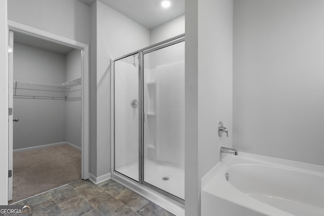 bathroom with a washtub, baseboards, a spacious closet, a shower stall, and stone finish flooring