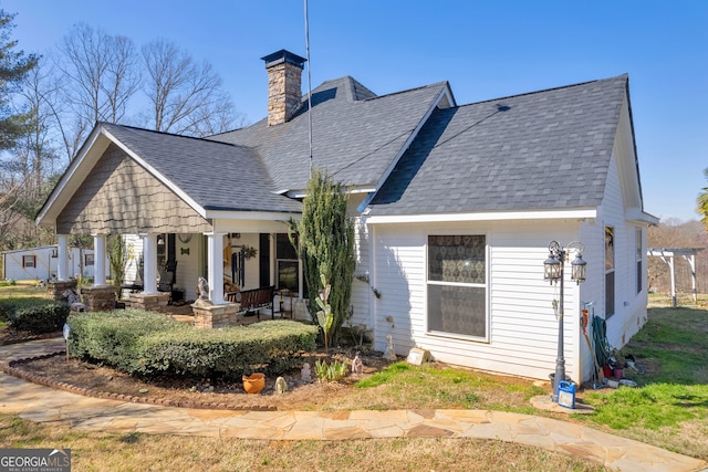 rear view of property featuring covered porch, roof with shingles, and a chimney