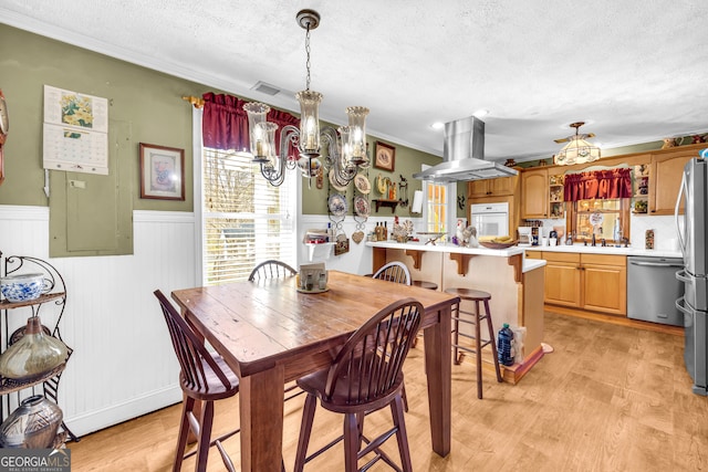 dining space with a textured ceiling, a notable chandelier, visible vents, light wood-style floors, and wainscoting