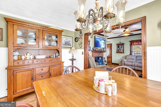 dining space featuring ornamental molding, a brick fireplace, wainscoting, and light wood-style flooring