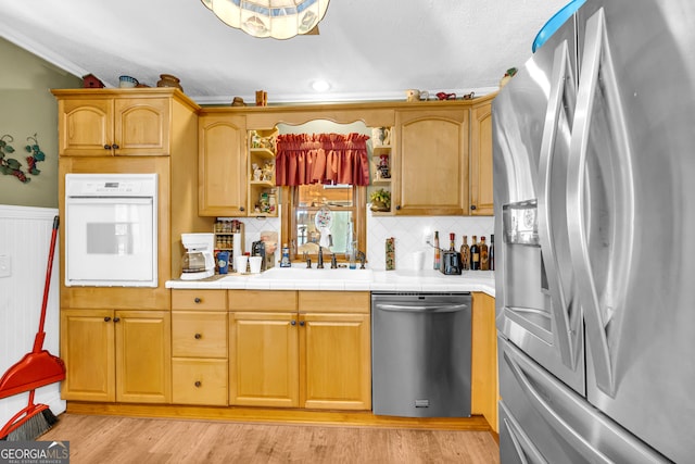 kitchen with appliances with stainless steel finishes, a sink, light wood-style floors, open shelves, and backsplash