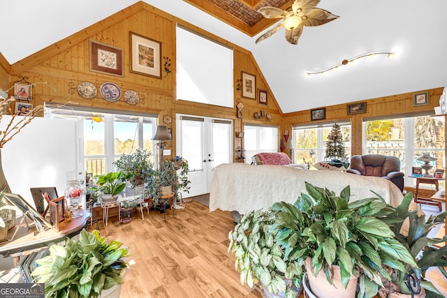 bedroom with high vaulted ceiling, light wood-type flooring, and wood walls