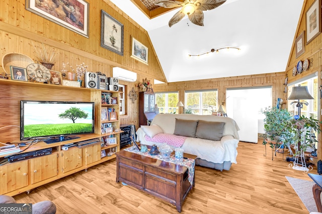 living room with wooden walls, a wall unit AC, ceiling fan, light wood-type flooring, and high vaulted ceiling