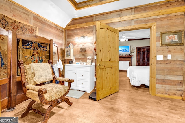 sitting room featuring vaulted ceiling, ceiling fan, light wood-type flooring, and wooden walls