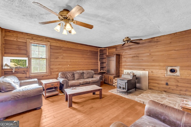 living area with a textured ceiling, ceiling fan, light wood-type flooring, and a wood stove