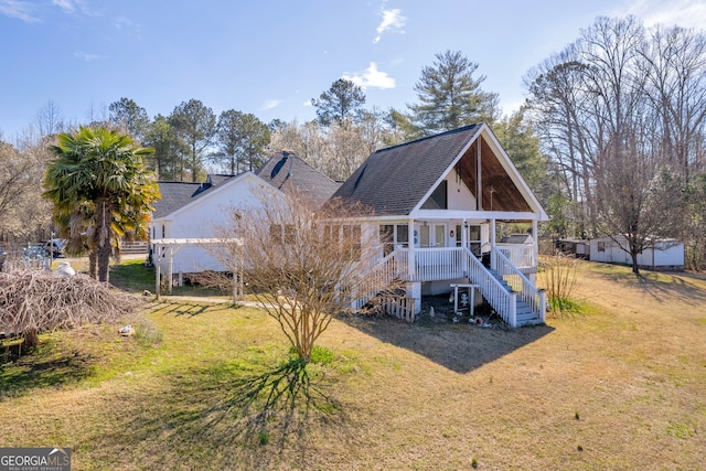 rear view of house featuring covered porch, roof with shingles, a lawn, and stairway