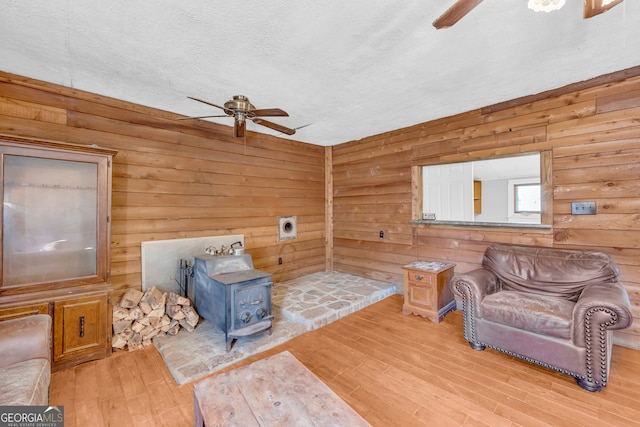 living area featuring wooden walls, ceiling fan, wood finished floors, a wood stove, and a textured ceiling