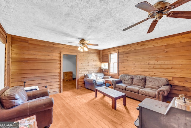 living area with light wood-style floors, wood walls, a textured ceiling, and a ceiling fan