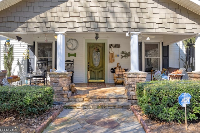 view of exterior entry featuring covered porch and a shingled roof