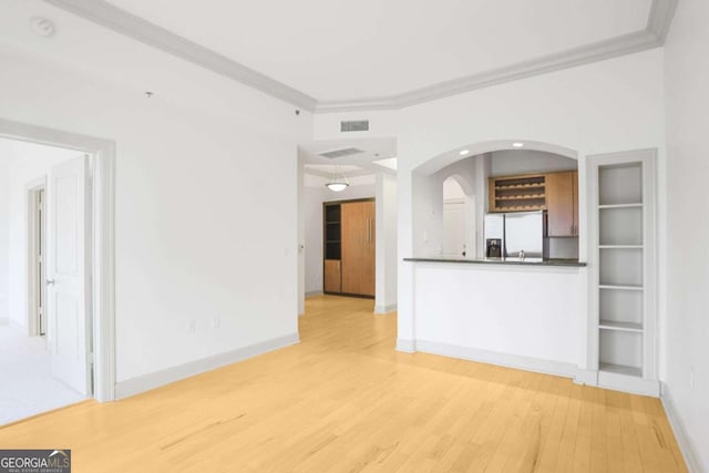 unfurnished living room with arched walkways, light wood-type flooring, baseboards, and ornamental molding