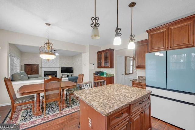 kitchen featuring a warm lit fireplace, dark wood-type flooring, a kitchen island, freestanding refrigerator, and brown cabinets