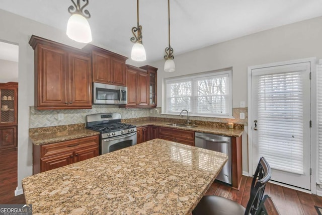 kitchen with light stone counters, a sink, appliances with stainless steel finishes, a center island, and tasteful backsplash