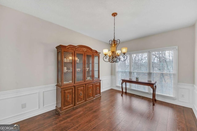 dining room with a chandelier, dark wood-type flooring, a wainscoted wall, and a decorative wall