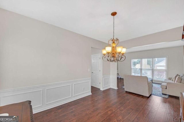 unfurnished dining area with a wainscoted wall, a notable chandelier, and dark wood finished floors