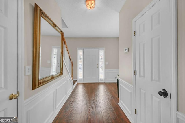 entryway with stairs, wainscoting, dark wood finished floors, and a decorative wall