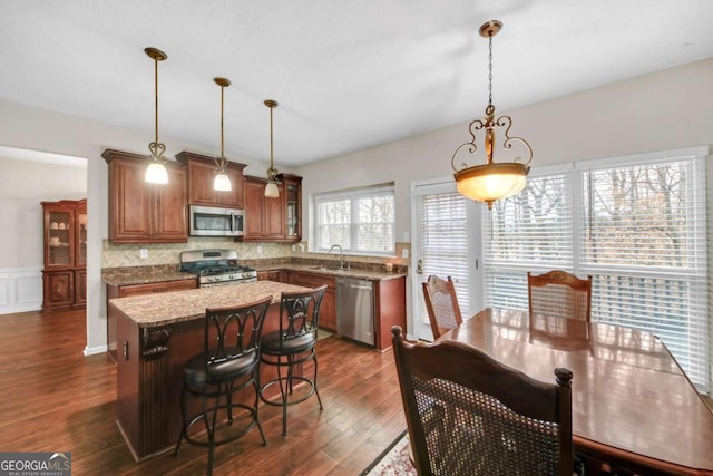 kitchen with dark wood finished floors, brown cabinets, a center island, stainless steel appliances, and a sink