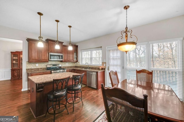 kitchen featuring brown cabinetry, dark wood finished floors, appliances with stainless steel finishes, a center island, and a sink