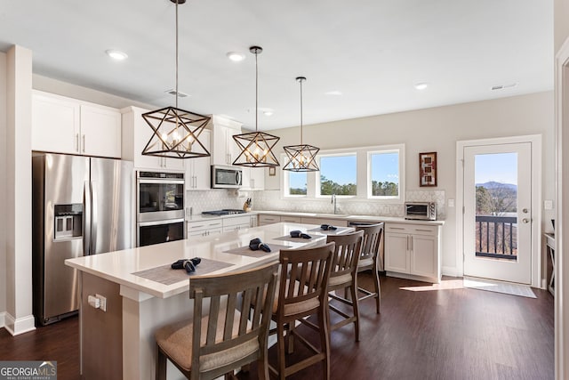 kitchen with dark wood-style flooring, white cabinetry, appliances with stainless steel finishes, backsplash, and a center island