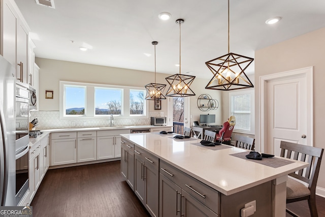 kitchen with dark wood-type flooring, a kitchen island, a sink, light countertops, and decorative backsplash