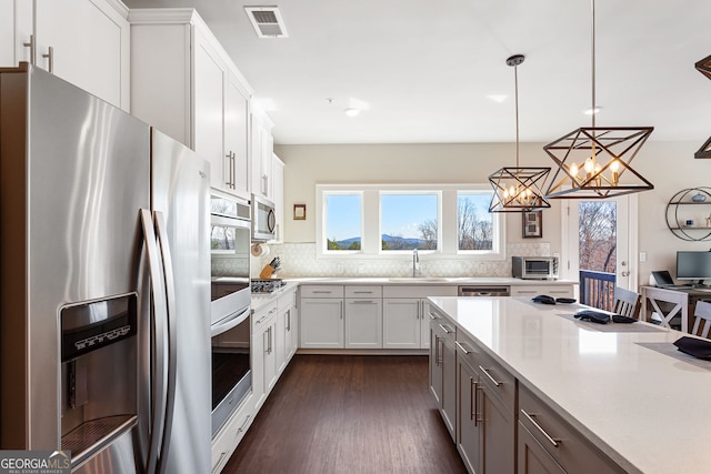 kitchen featuring visible vents, appliances with stainless steel finishes, a sink, light countertops, and backsplash