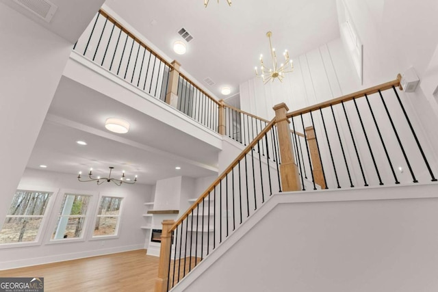 stairway featuring visible vents, a high ceiling, wood finished floors, a chandelier, and baseboards