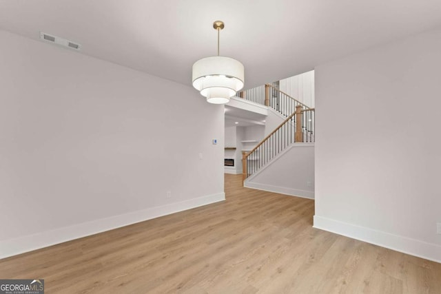 interior space featuring a fireplace, wood finished floors, visible vents, baseboards, and stairway