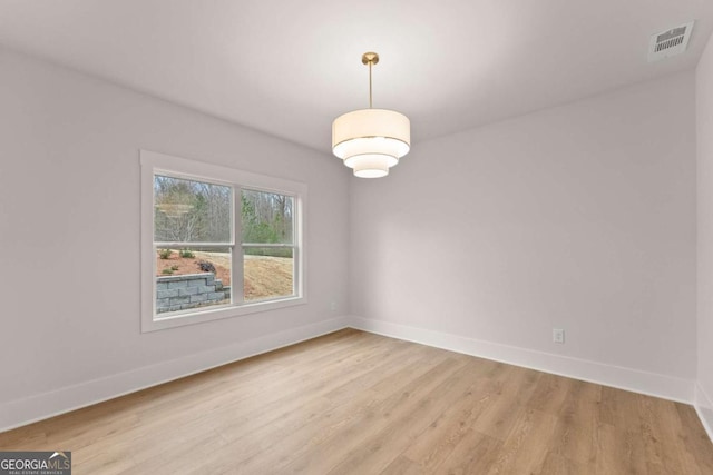 empty room with baseboards, visible vents, and light wood finished floors